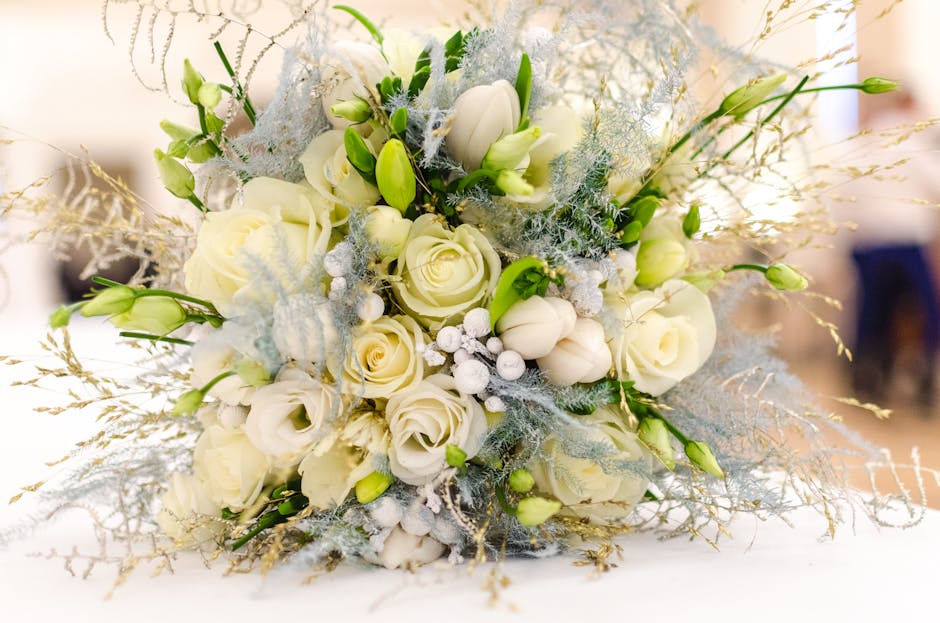 A collection of floral arrangements featuring white hydrangeas, pink spray roses, blue eryngium, yellow solidago, and small white baby's breath, all displayed in clear glass vases wrapped with pink an