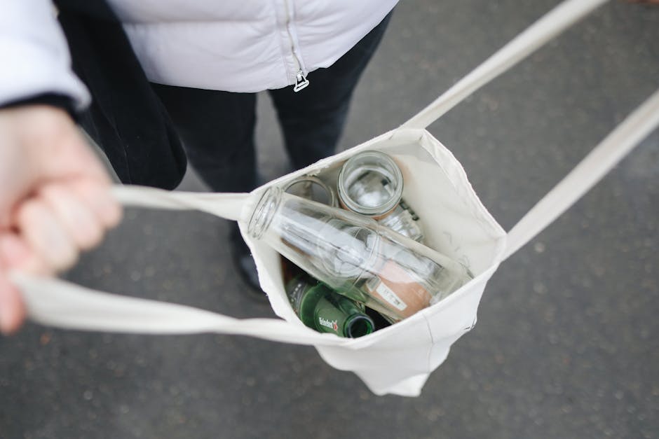 This image shows a person's hand holding a piece of crumpled white paper or tissue next to a white bowl filled with used floral wrapping, such as paper, ribbon, and other packaging materials, indicati