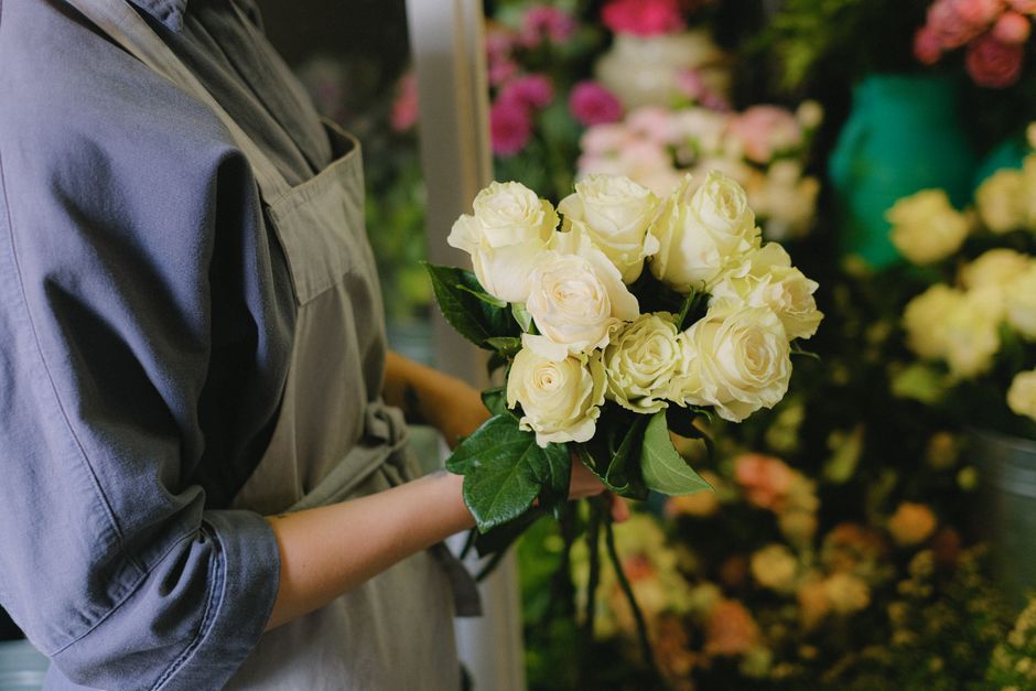 A close-up image of a large bouquet of fresh pink roses with tightly layered petals, arranged on a white surface. The roses vary in shades from light pink to deeper magenta, and some are still in bud